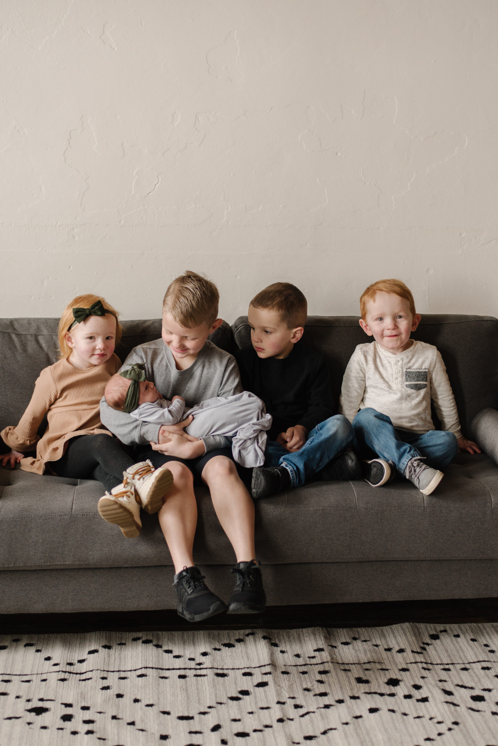 Four older siblings sit on a couch and hold new sister.