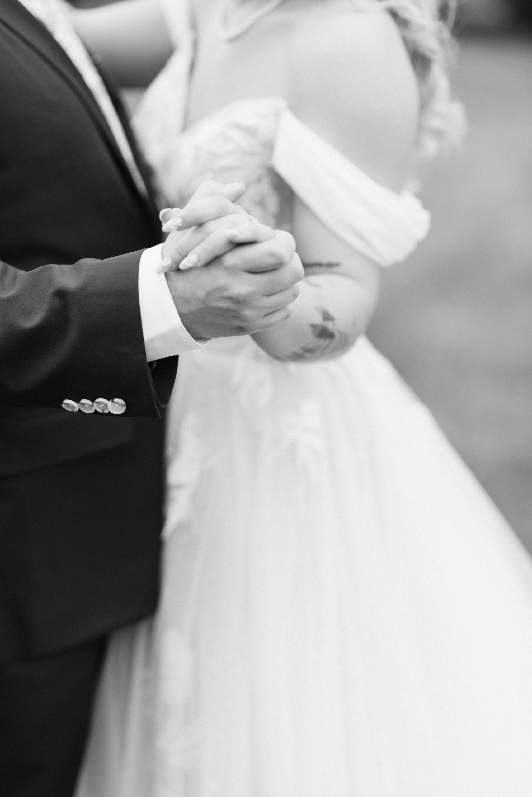 Black and White image of a couple on their wedding day holding hands outside of a barn while they dance.